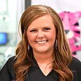 Woman smiling at camera in professional dental office setting with colorful background.