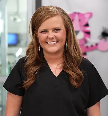 Woman in black scrubs smiling at camera in bright dental office setting.