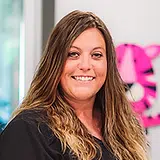 Woman smiling at camera in professional dental office setting with pink flowers visible in background.