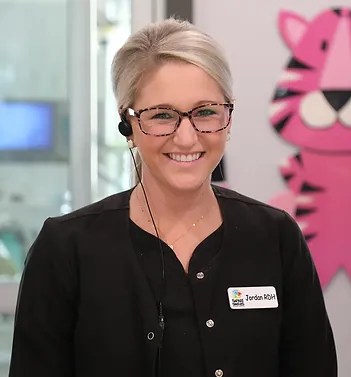 Smiling dental professional wearing glasses and name badge in modern dental office setting.