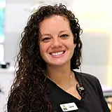 Smiling woman with curly dark hair wearing black uniform in dental office setting