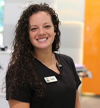 Smiling female dental staff member wearing black scrubs with name badge in dental office.