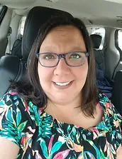 Woman smiling at camera wearing glasses in car, colorful patterned shirt