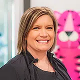 Woman smiling at camera in front of pink dental office signage, professional headshot setting.