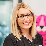 Woman with blonde hair and glasses smiling at camera in dental office setting.