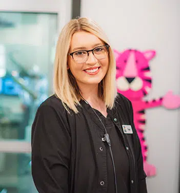 Female staff member smiling at camera in modern dental office with pink decorative element visible behind her.