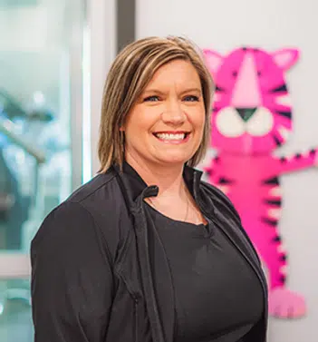 Woman smiling at camera in dental office with pink tiger logo visible in background.