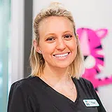 Blonde woman smiling at camera wearing black shirt in dental office setting with pink decorations
