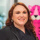 Woman smiling at camera in professional portrait with pink background for dental practice
