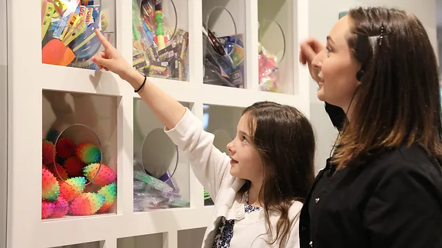 Two people examining children's dental artwork displayed on a white wall shelf in a pediatric dental office.