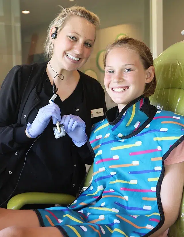 Dental professional and young child smile together in pediatric dental office setting.