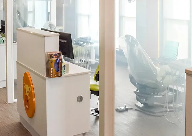 Modern pediatric dental office reception area with white desk overlooking city skyline through floor-to-ceiling windows.
