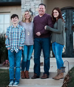 Family of five smiling together outdoors in front of their home.