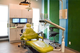 Colorful pediatric dental operatory with yellow chair, green walls, and modern equipment for children's dental care.