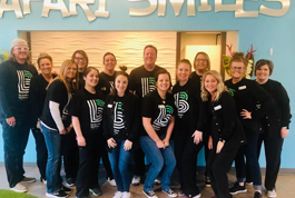 Team of dental professionals in black uniforms posing together at Safari Smiles Children's Dentistry clinic.