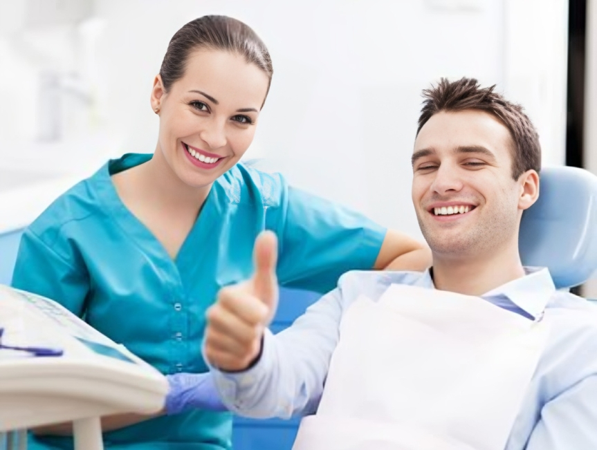 Pediatric dentist in blue scrubs and patient giving thumbs up in modern dental office.